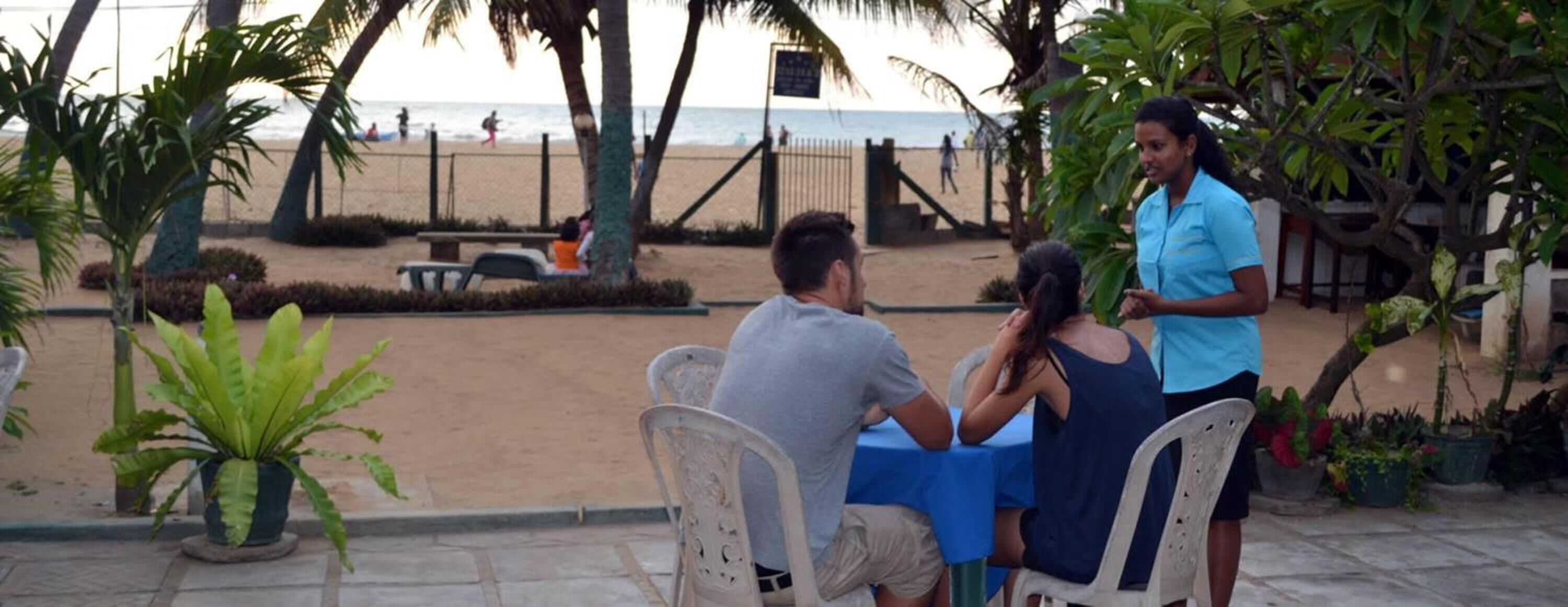 A patio area with outdoor seating, a view of the beach, and palm trees.