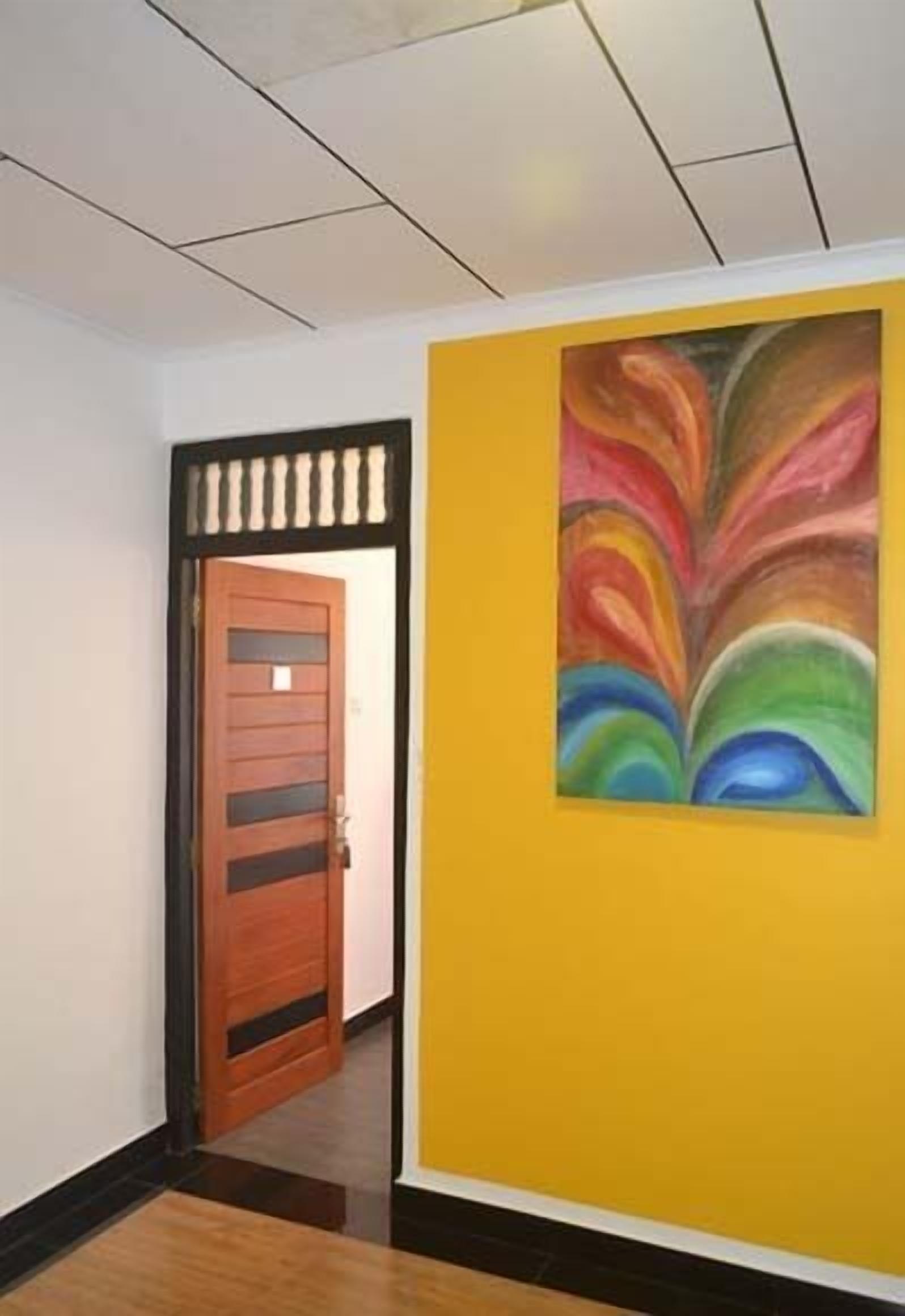 Un pasillo con una puerta de madera y una pared amarilla decorada con un cuadro abstracto y colorido.