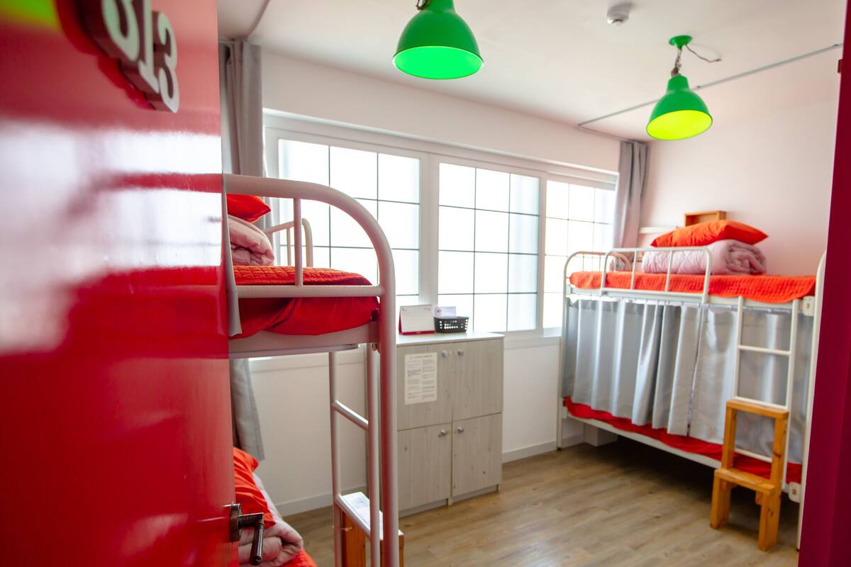 A bunk bed room with a window, a desk, and a green hanging lamp.