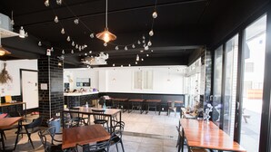 A restaurant interior with multiple tables and chairs, a black brick column, and string lights on the ceiling.