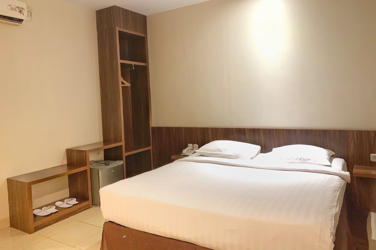 A hotel room with a bed, a wardrobe, a bedside table, and a shoe rack.