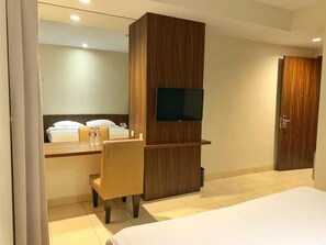 A hotel room with a bed, a desk with a chair, a television mounted on the wall, and a door. - Ameera Hotel (Pekanbaru)