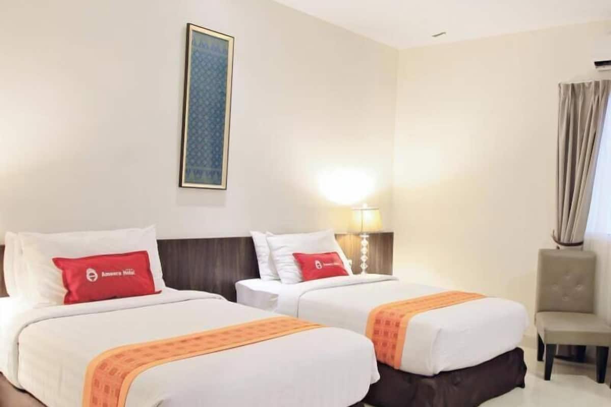 A hotel room with two beds, a nightstand with a lamp, a chair, and a framed picture on the wall.