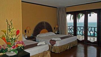A hotel room with two beds, a large window with a view of the ocean, and a balcony with a railing.