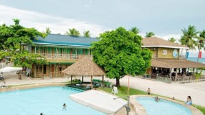 Une piscine avec plusieurs couloirs, un espace de détente avec des fauteuils et un bâtiment avec un toit végétalisé en arrière-plan.