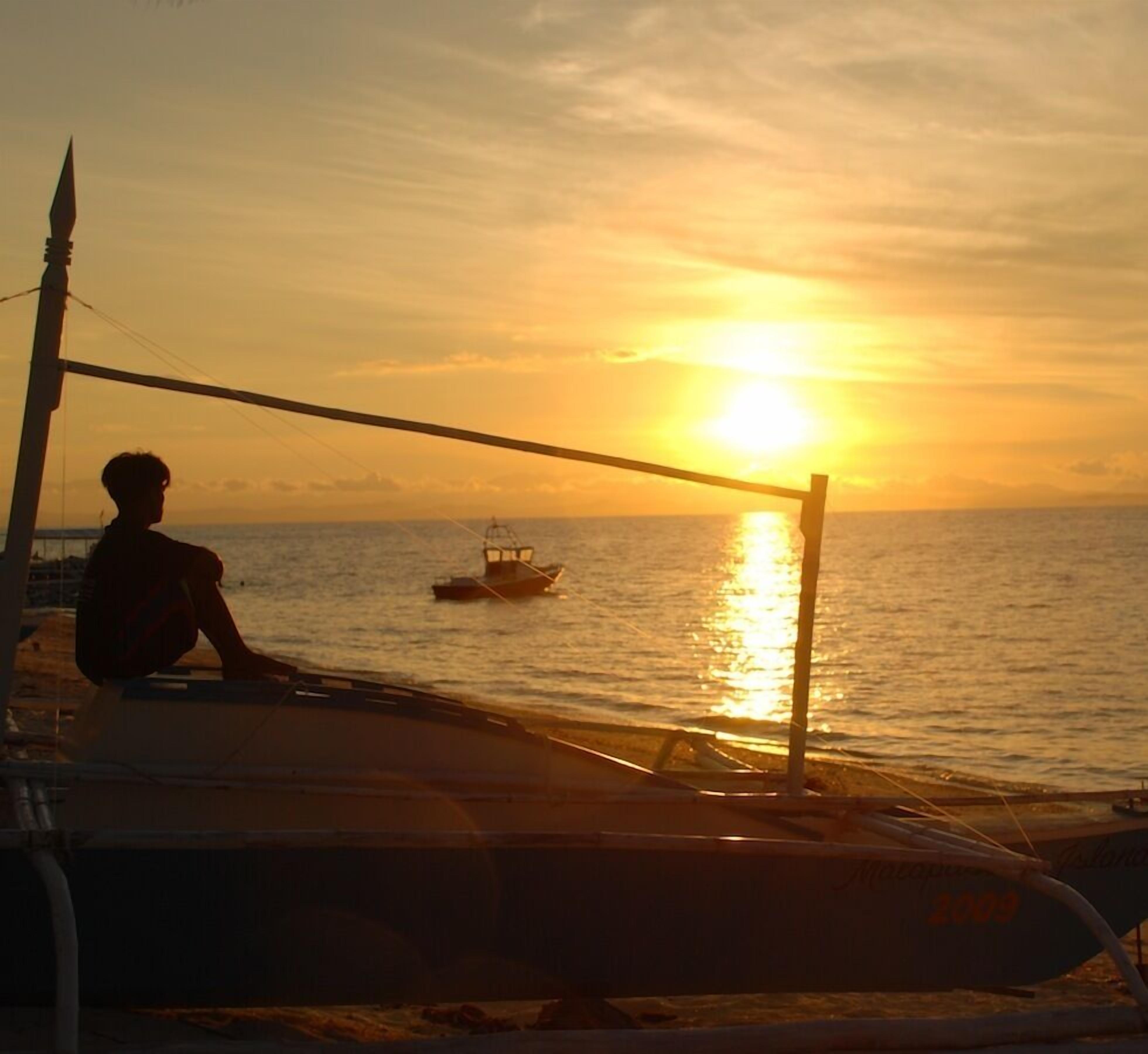 Une personne assise sur un bateau, contemplant le coucher de soleil sur l’océan.