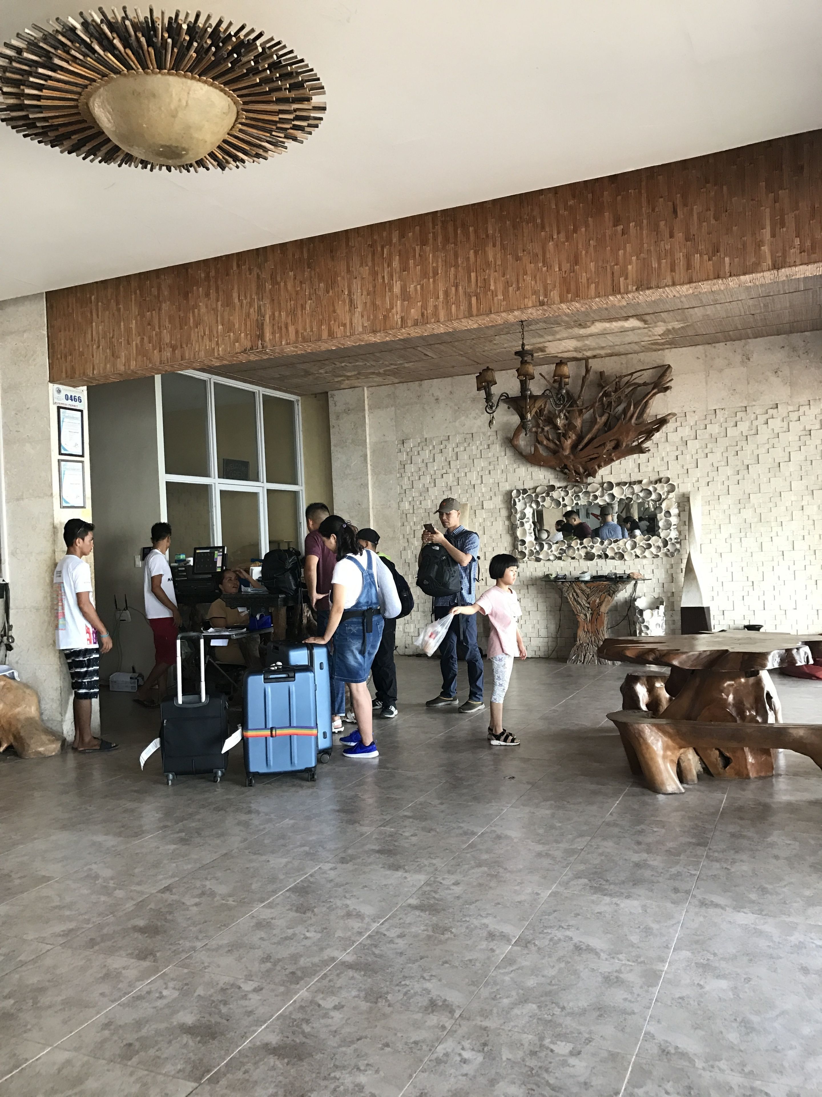 A spacious lobby with a modern design, featuring a large wooden ceiling, a decorative wall with a unique pattern, and a central area with a wooden table and chairs.