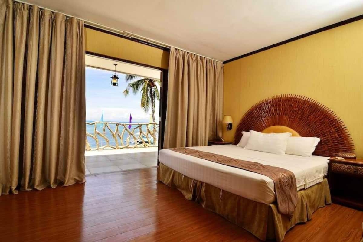A hotel room with a large bed, a wooden headboard, a nightstand, and a view of the beach.
