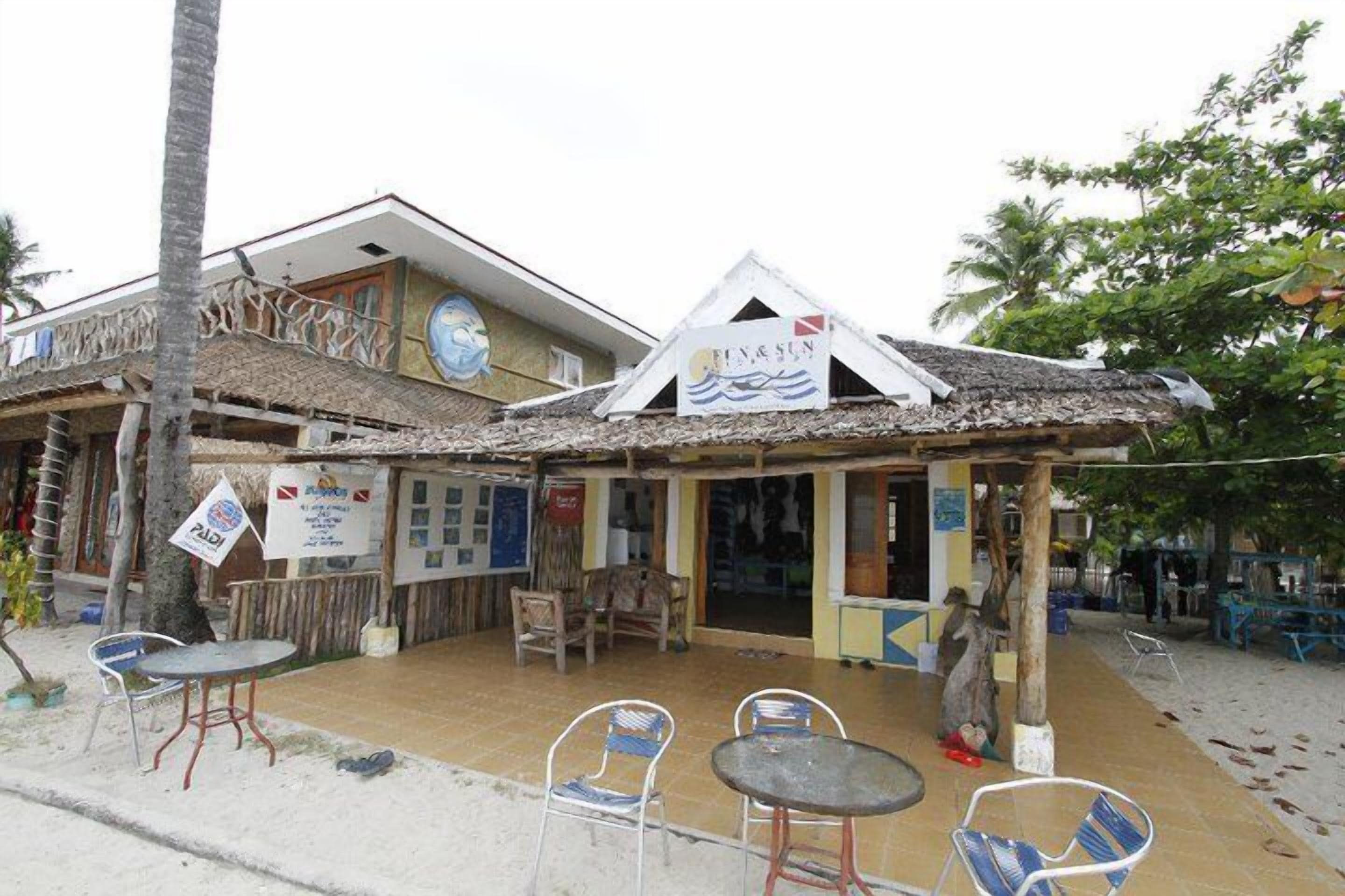A beachside café with outdoor seating, a thatched roof, and a sign reading "Café & Sun".