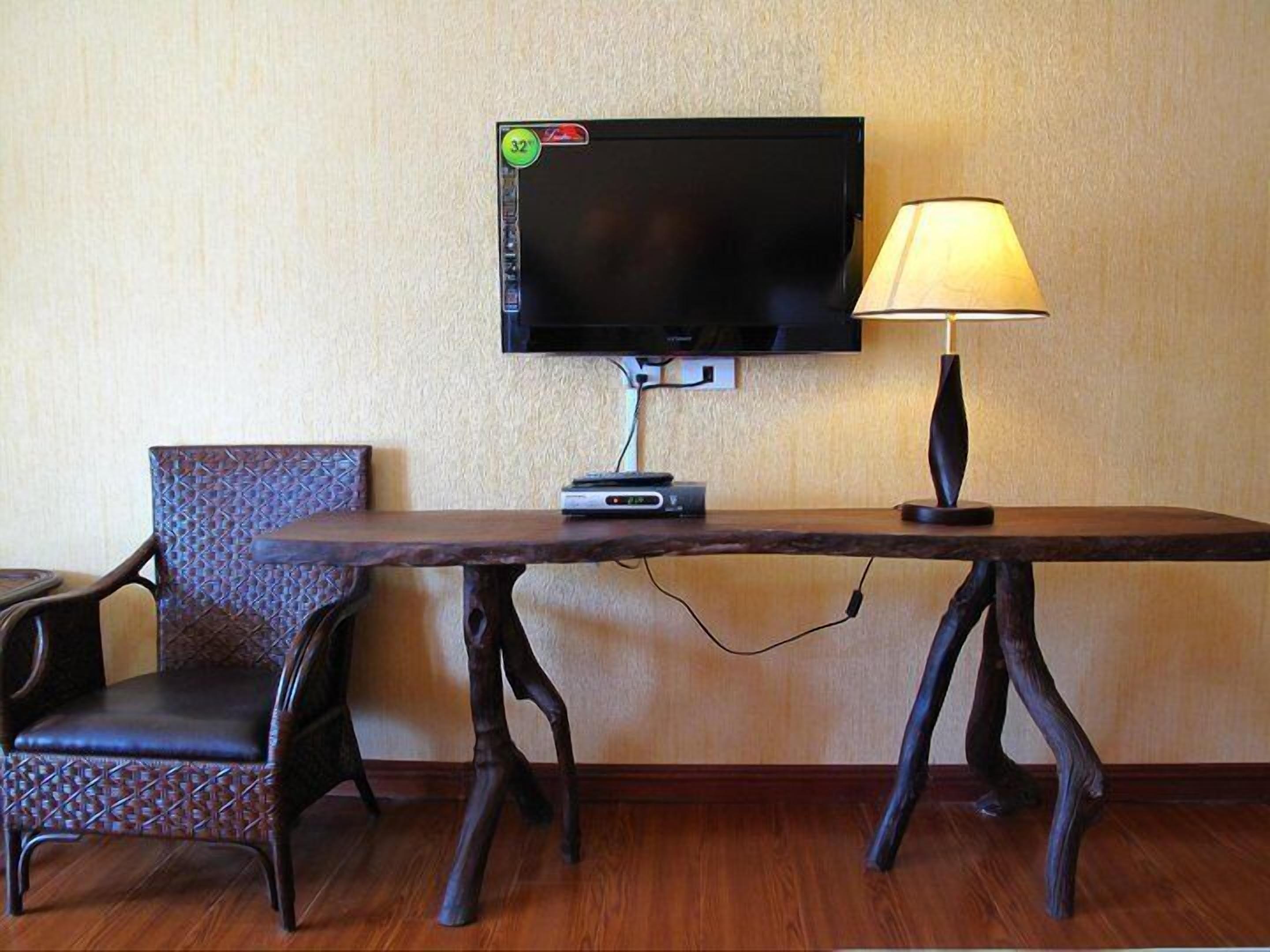 Une chambre d’hôtel dotée d’un téléviseur à écran plat fixé au mur, d’une table en bois avec une lampe et d’une chaise à motifs.