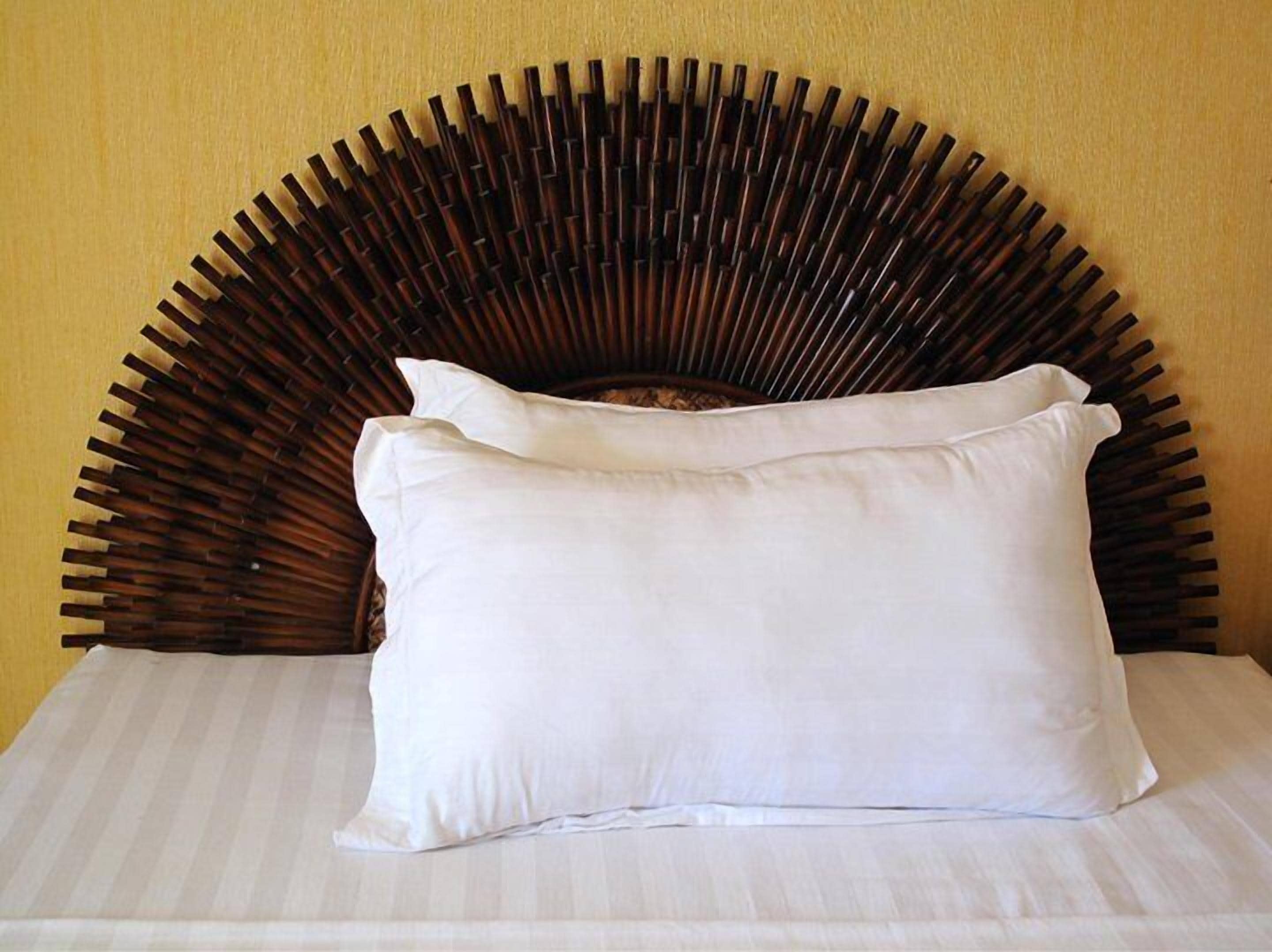 A bed with a white pillow and a headboard with a bamboo-like design.
