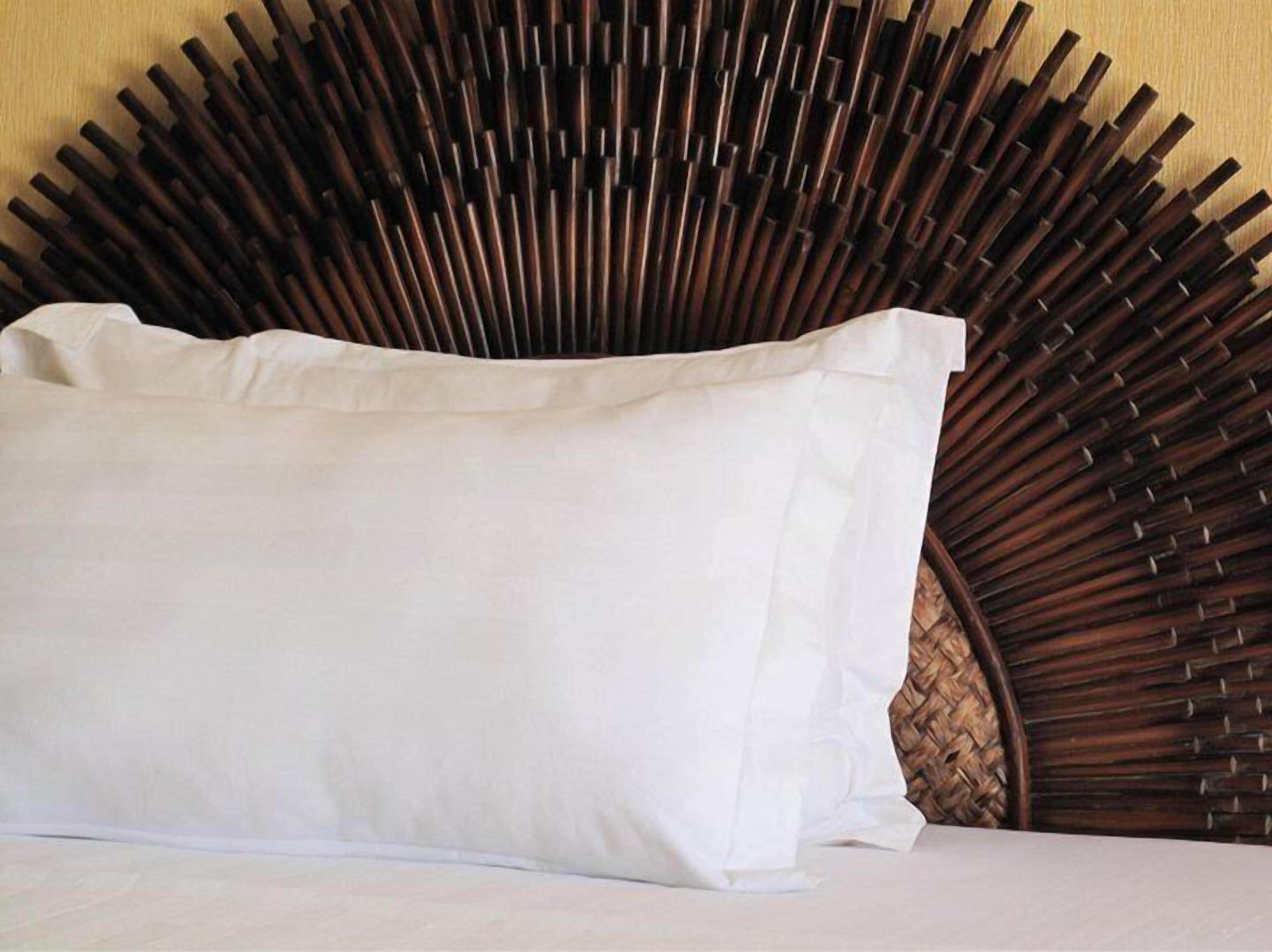 Una cama con almohada blanca y cabecera con diseño que recuerda a la caña de bambú.