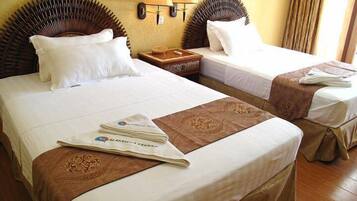 Two double beds with white linens, a wooden nightstand, and a wall-mounted lamp between them.
