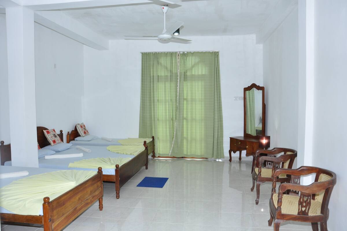 Une chambre avec deux lits en bois, un ventilateur de plafond, un miroir et un rideau vert.