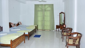 Une chambre avec deux lits en bois, un ventilateur de plafond, un miroir et une chaise.