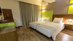 Habitación de hotel con dos camas, un escritorio de madera, un espejo y una ventana con cortinas.