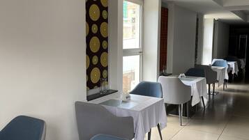 A hotel room with a bed, a small table, and a chair. There is a window with a view of buildings outside.