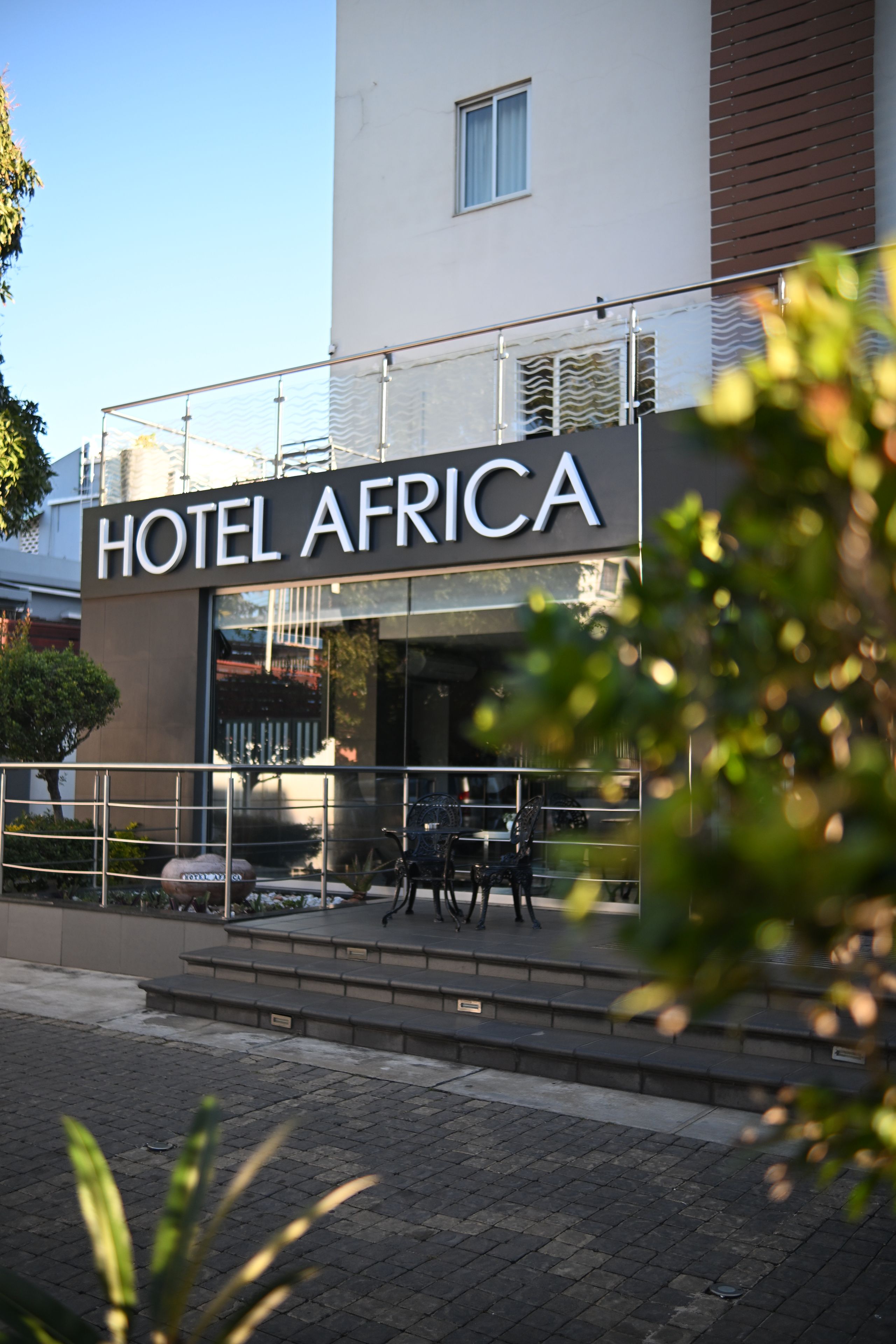 Une enseigne d’hôtel indiquant « HÔTEL AFRIQUE », avec des places assises à l’extérieur et un escalier menant à l’entrée.