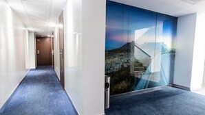 Un pasillo con alfombra azul, un muro de cristal con paisaje de montaña y un bote de basura.