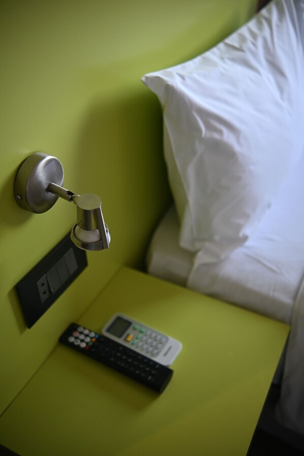 A bed with a white pillow and a green wall. There is a remote control and a door lock on the nightstand.