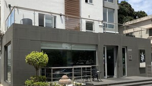 Un hotel moderno con fachada de vidrio, un pequeño jardín con un árbol y rocas, y un letrero que indica la habitación 1103.
