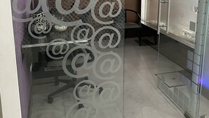 Un espacio de oficina moderno con un separador de vidrio que muestra símbolos decorativos de correo electrónico, una pizarra y una silla de oficina negra.
