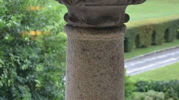 A stone column with intricate carvings, set against a backdrop of a well-manicured garden and a road.