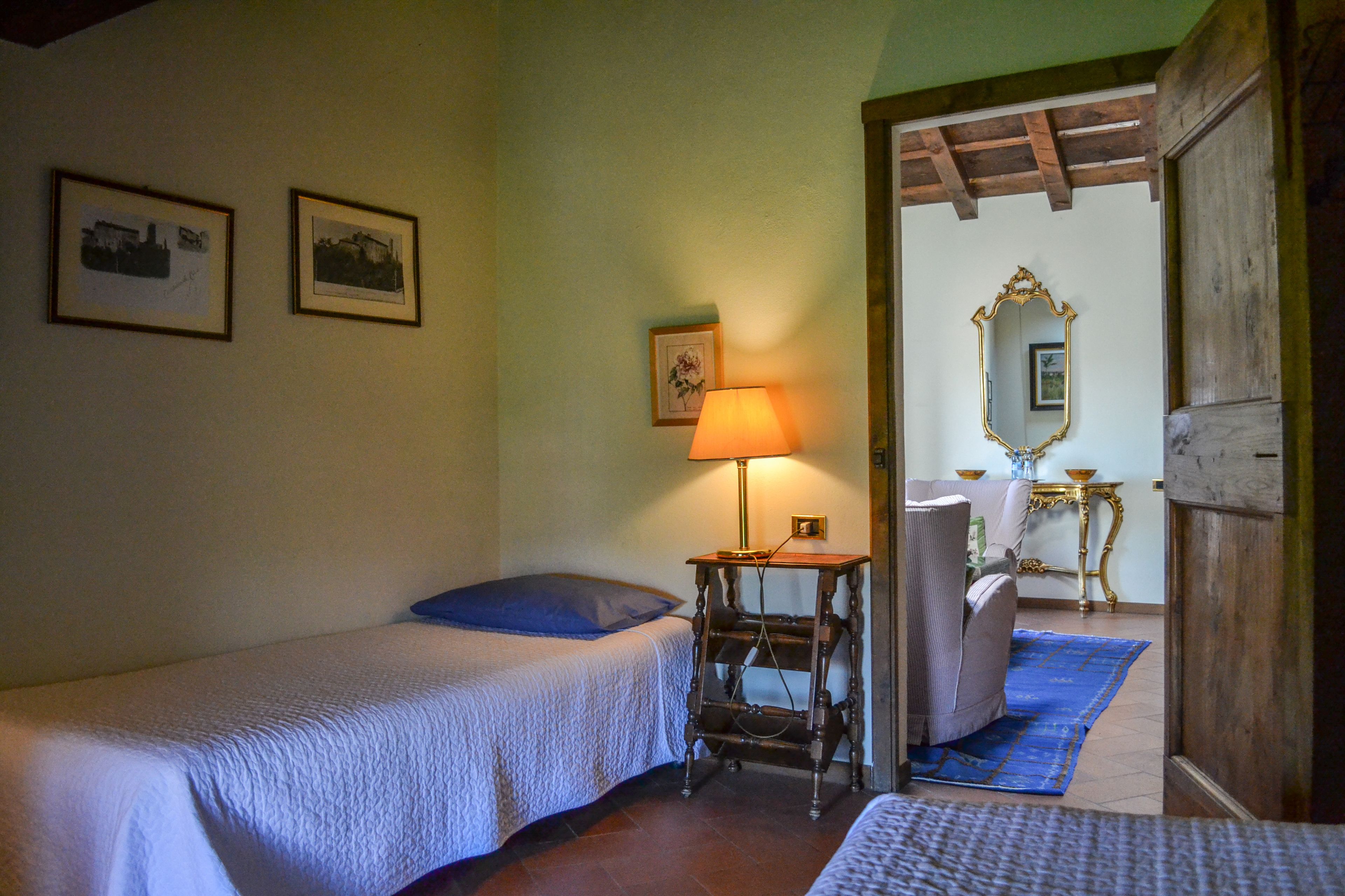 A bedroom with two beds, a nightstand, a lamp, and a wooden door leading to another room.