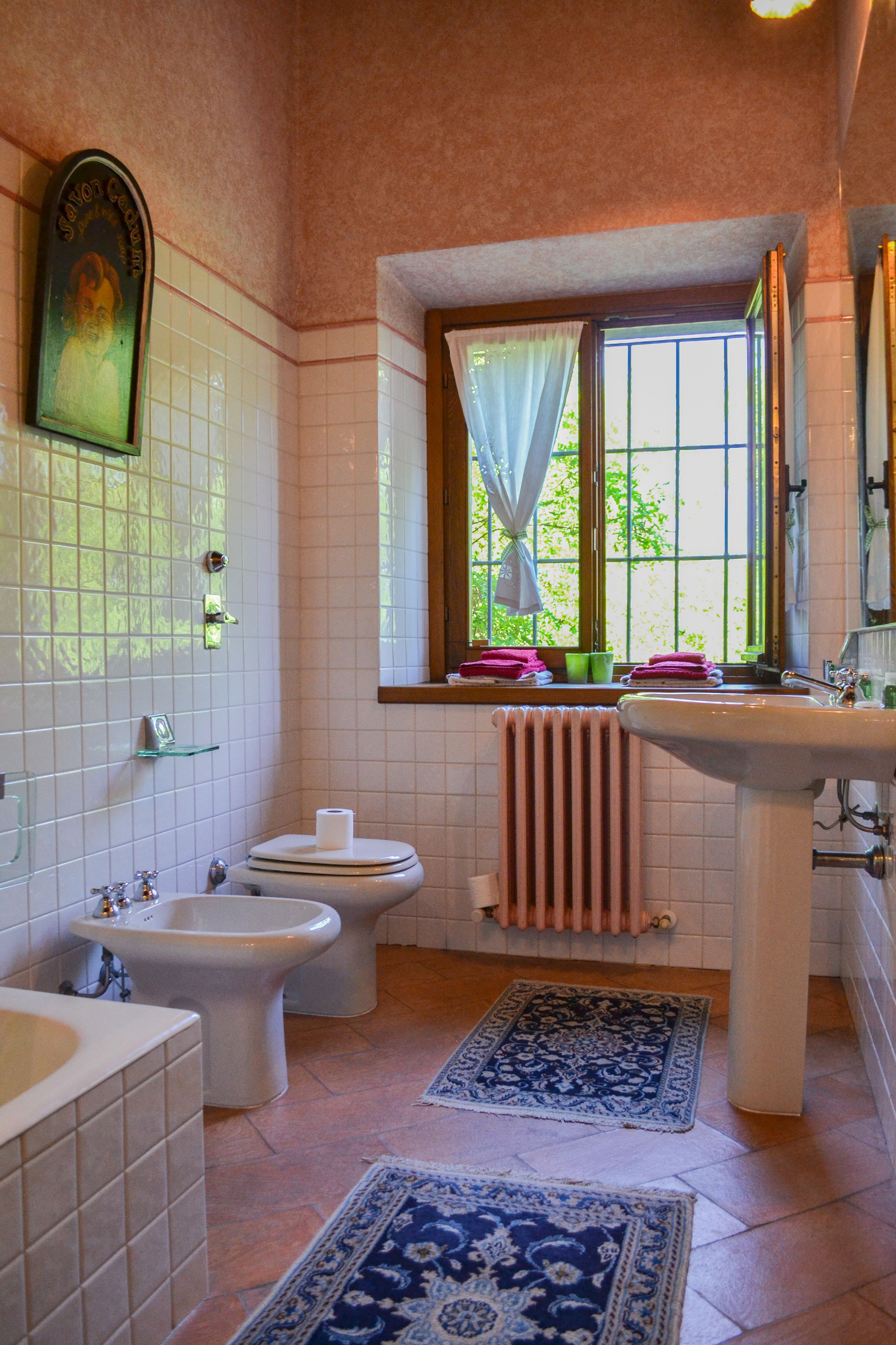 Un bagno con toilette, bidet, lavandino e finestra con tende.