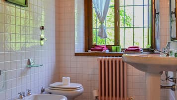 Un bagno con toilette, bidet, lavandino e finestra con tende.