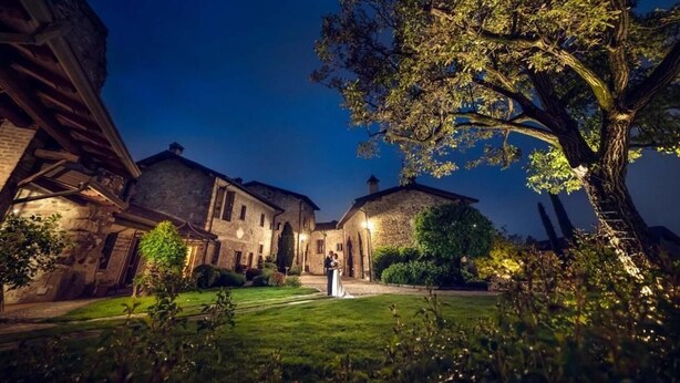 Un patio con edificios de piedra, un árbol grande y una pareja con traje de boda.