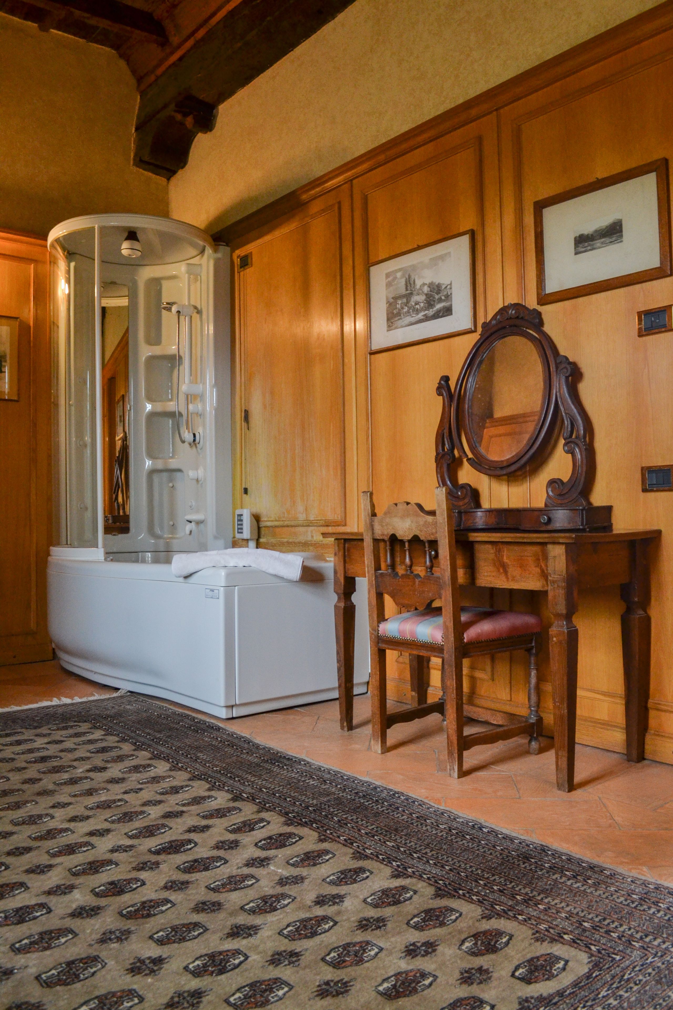 A room with a bathtub, a wooden chair, a mirror, and framed pictures on the wall.