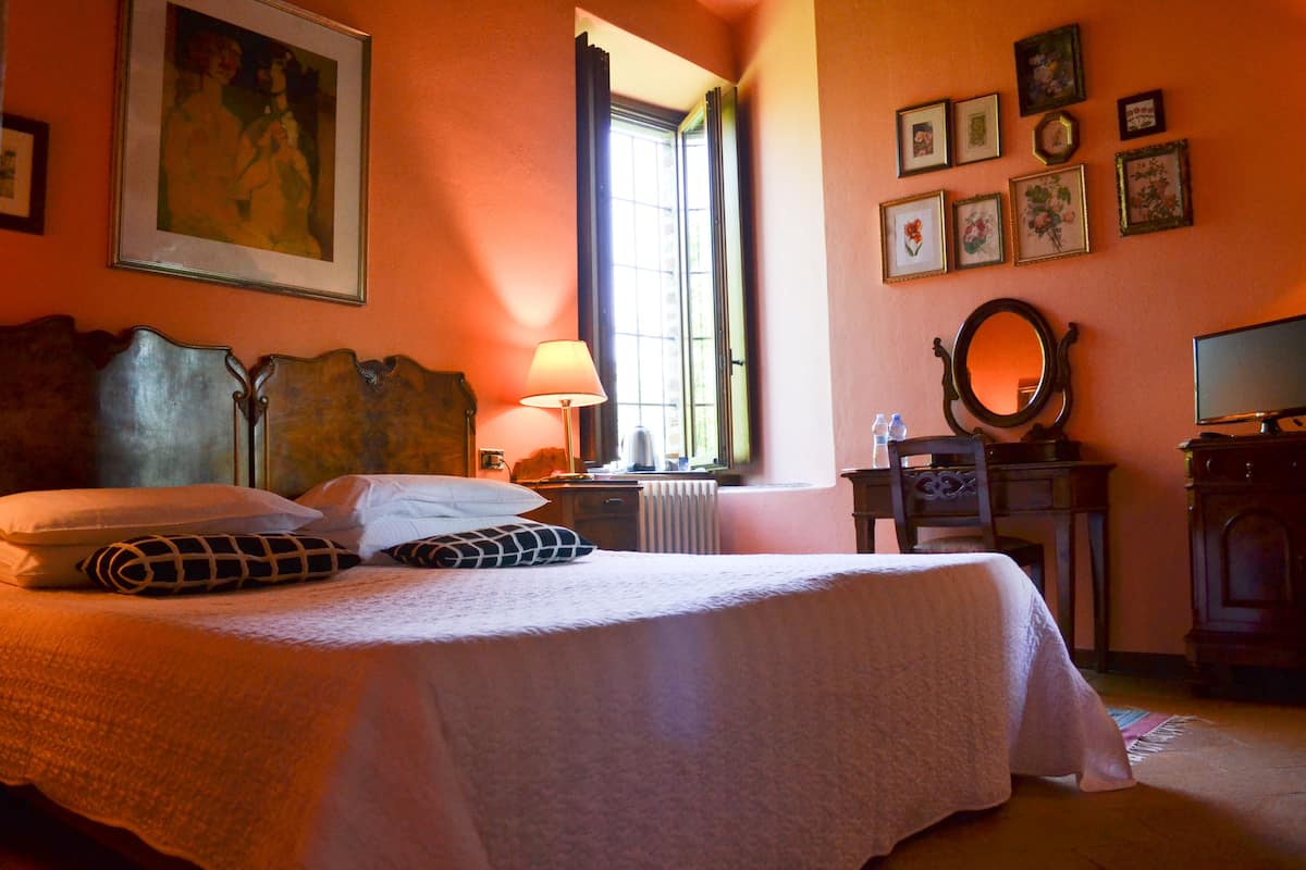 Un lit bien fait, avec des oreillers, une lampe de chevet, une commode avec un miroir et des tableaux encadrés accrochés au mur.