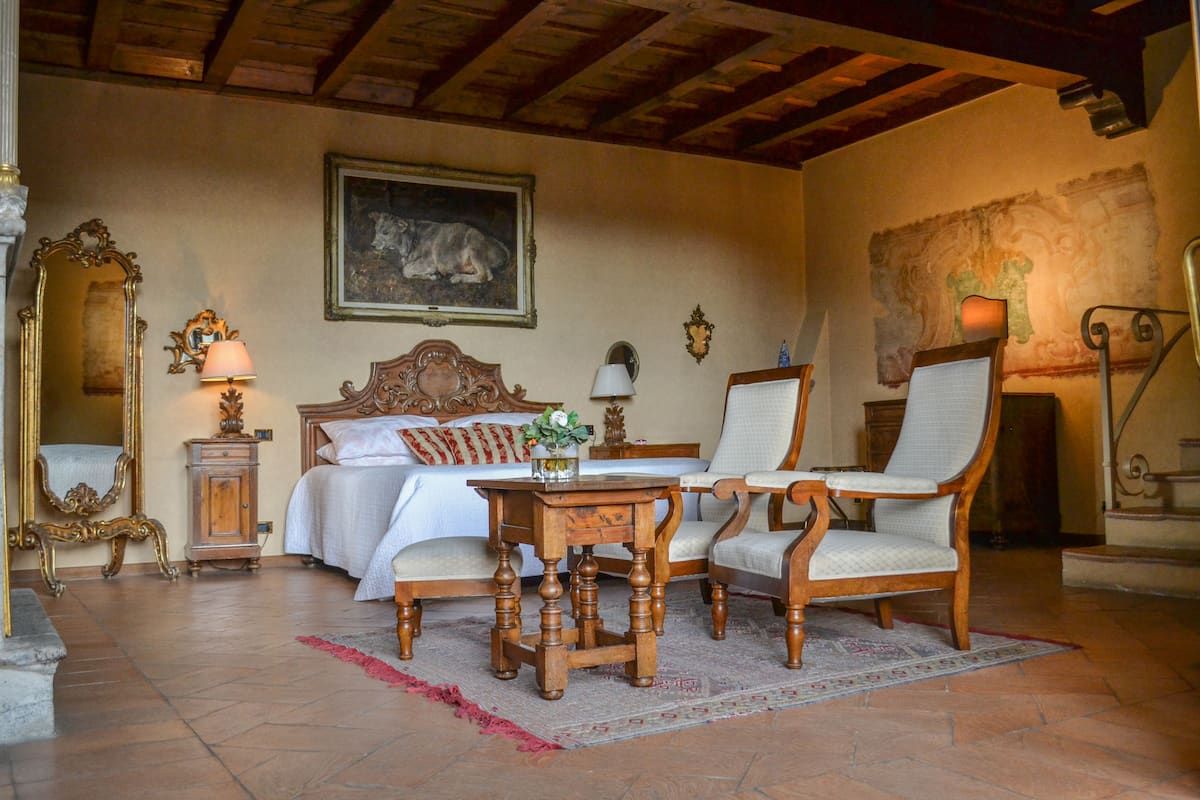 Une pièce comprenant un lit, deux chaises, une table, un miroir et un tableau accroché au mur.