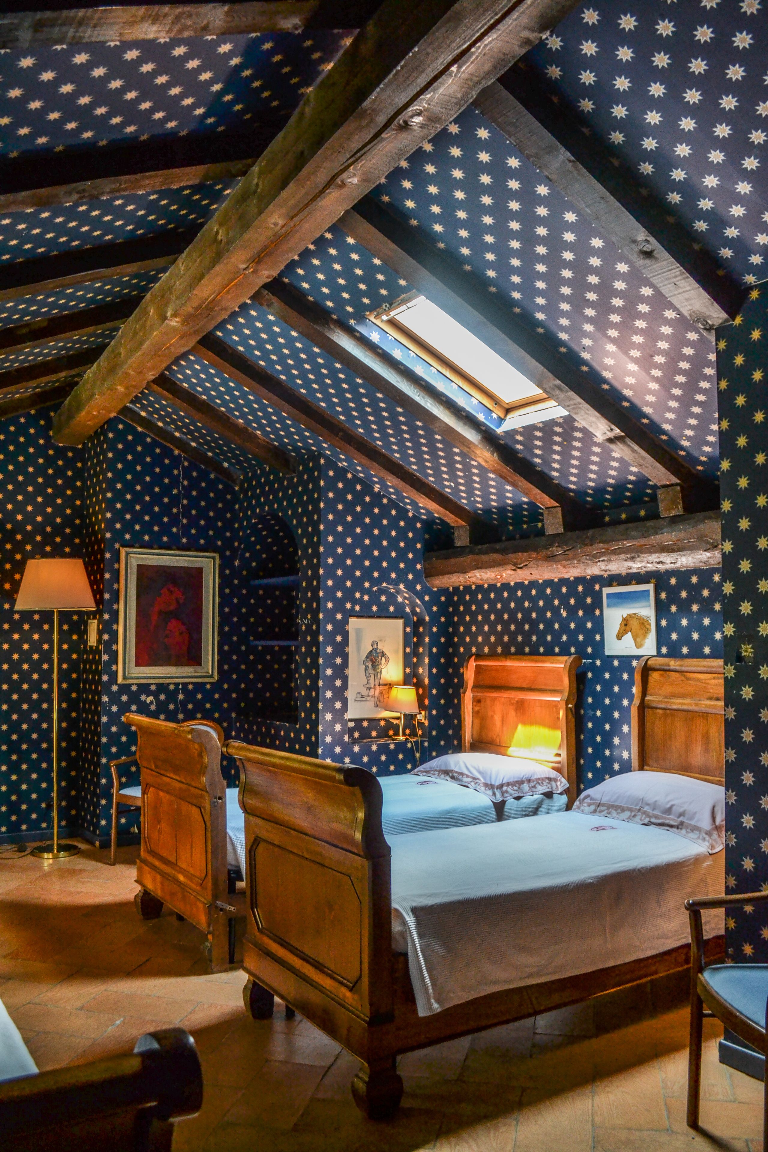 A room with a sloped ceiling, wooden beams, and a bed with a headboard.