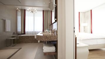 A modern hotel room with a large bed, a bathroom with a sink and mirror, and a view of the city.
