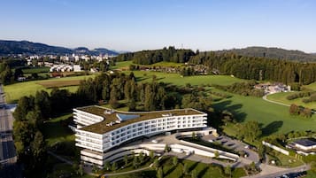 A modern hotel with a curved roof, surrounded by green fields and a golf course.