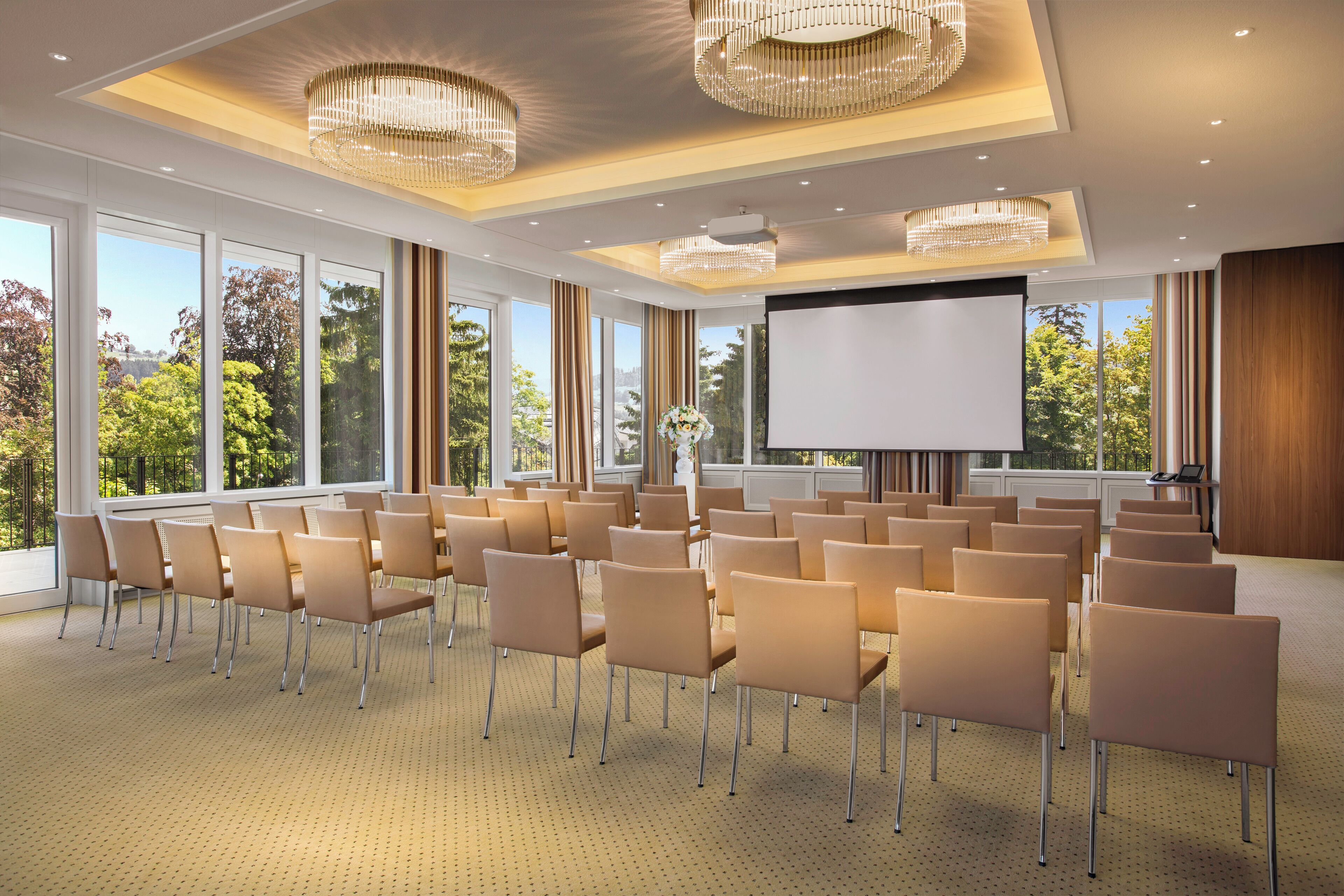 Un salón de conferencias con filas de sillas, una pantalla grande y candelabros.