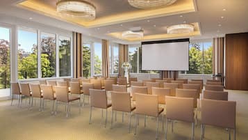 Un salón de conferencias con filas de sillas, una pantalla grande y candelabros.