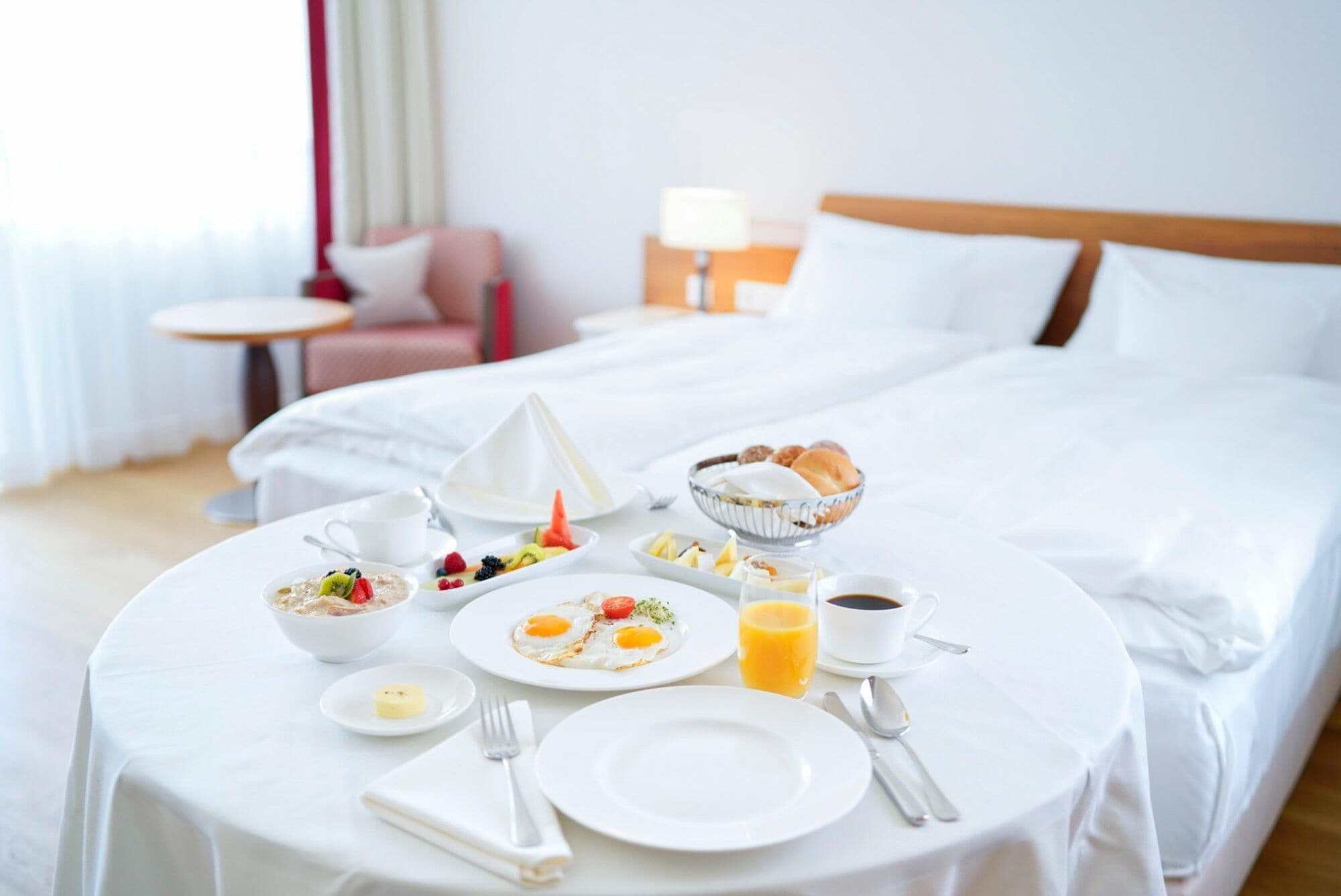 Ein ordentlich gedeckter Frühstückstisch mit verschiedenen Speisen, darunter Eier, Früchte und Gebäck, in einem Hotelzimmer.