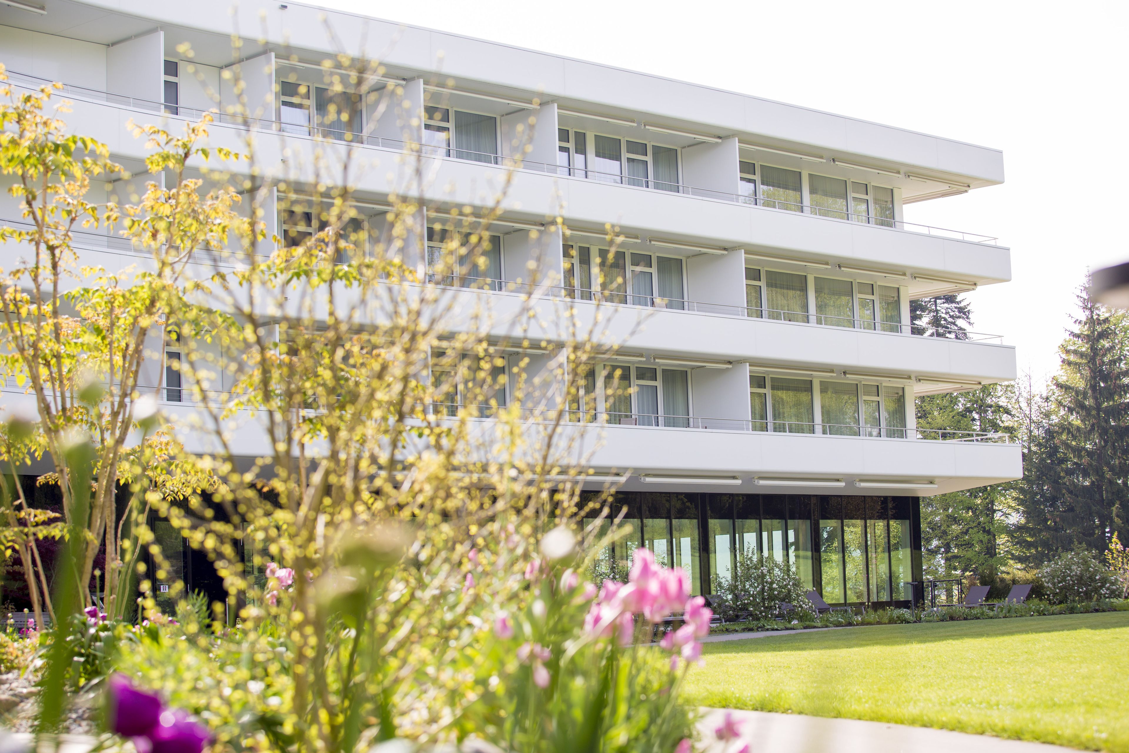 Ein modernes Mehrgeschosshaus mit Balkonen und großen Fenstern, umgeben von einem gepflegten Garten mit verschiedenen Pflanzen und Blumen.