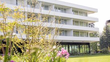 Ein modernes Mehrgeschosshaus mit Balkonen und großen Fenstern, umgeben von einem gepflegten Garten mit verschiedenen Pflanzen und Blumen.