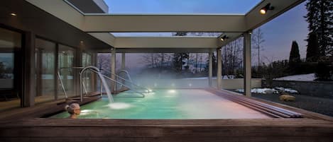 Un spa moderne doté d’un jacuzzi à ciel ouvert, d’une terrasse en bois et offrant une vue sur le paysage environnant.