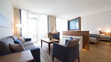 Una habitación de hotel moderna con sofá, sillón, mesa de comedor y televisor montado en la pared.