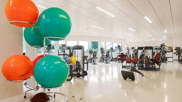 A gym with exercise equipment, large windows, and colorful exercise balls.