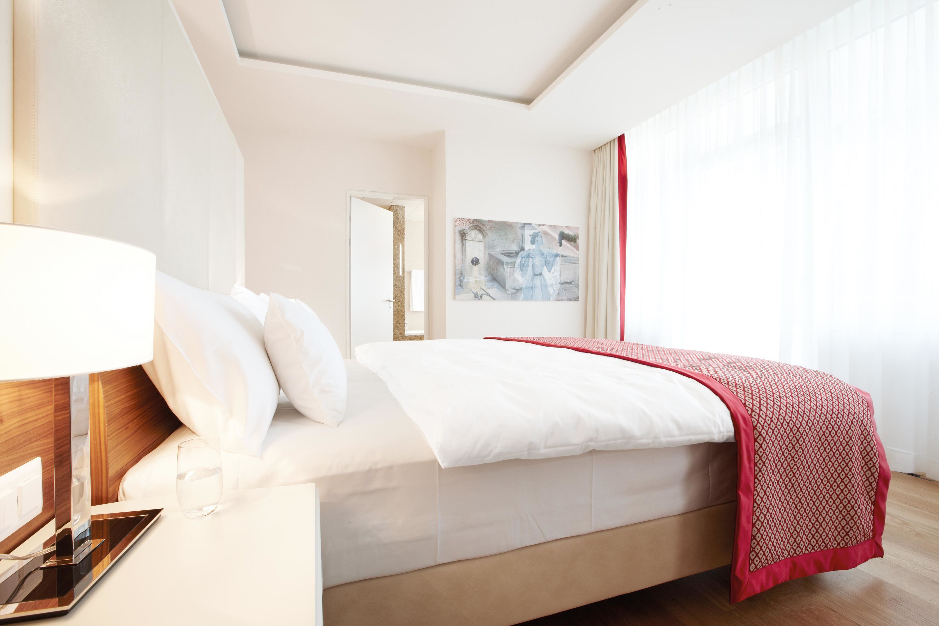 Una camera d'albergo moderna con un letto rifatto, un comodino con una lampada e un quadro appeso al muro.