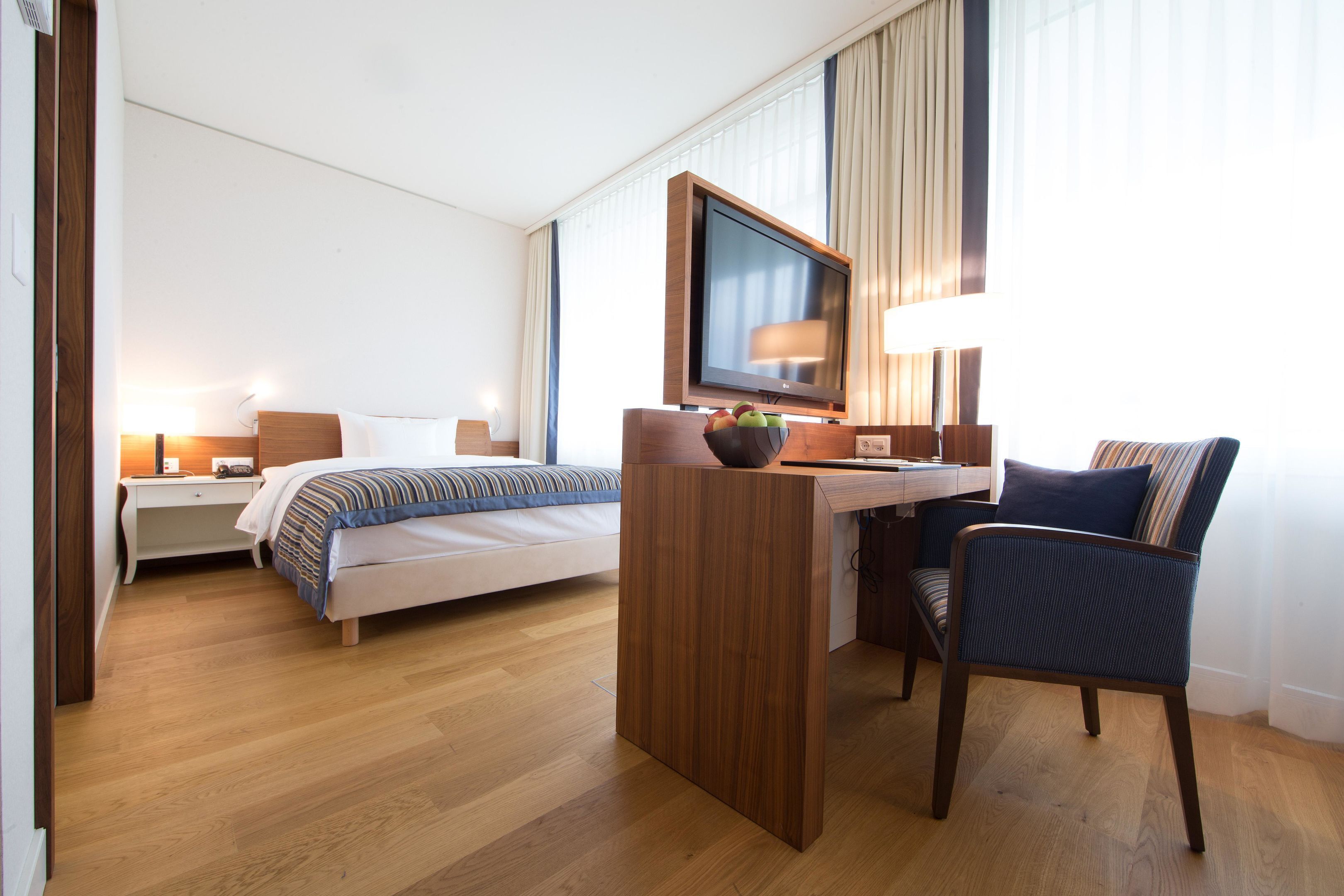 A hotel room with a bed, desk, chair, TV, and lamp.