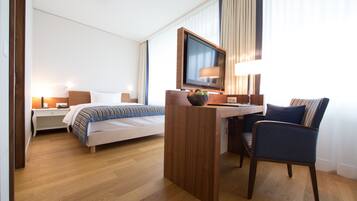 A hotel room with a bed, desk, chair, TV, and lamp.