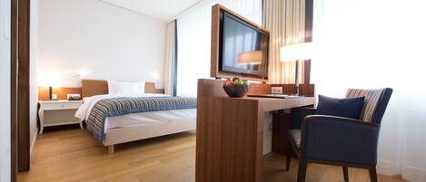 Habitación de hotel con cama, escritorio, silla, televisión y lámpara.