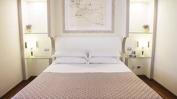 Een net opgemaakt bed met een bedsprei met dessin, twee nachtkastjes met lampen en een lijstwerk aan de muur.